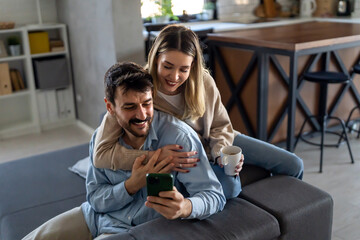 Smiling couple embracing while looking at smartphone. People sharing social media on smart phone.