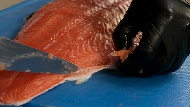 Cutting raw salmon fillet. The cook cuts off the unusable parts of the fish.