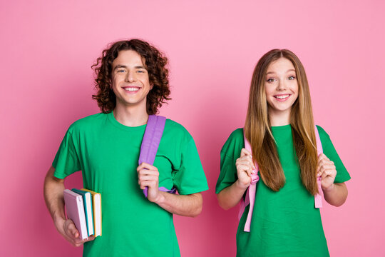 Portrait of happy couple teenagers wear green t shirt bring backpacks and literature to prepare exams isolated on pink color background