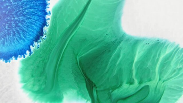 Close-up of vibrant blue and green ink patterns merging in water, creating an abstract art effect