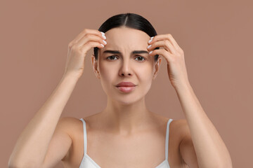 Woman with dry skin checking her face on beige background