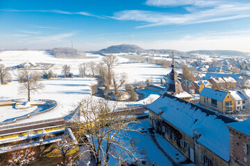 Aerial view of a winter landscape over the rooftops of the Chateau Neercanne castle and a valley just outside Maastricht, covered with fresh snow with a winding river through the scene and the slopes - Powered by Adobe