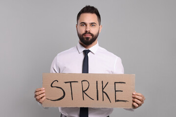 Young man holding cardboard banner with word Strike on light grey background