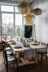 Happy easter dinner with decor at home. Minimalist composition in living room with copy space, hanging lamp, candle, easter eggs, vase with twig, branch, leaves. Interior design of easter dining room