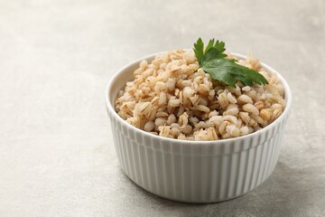 Tasty pearl barley porridge in bowl on light textured table, closeup. Space for text