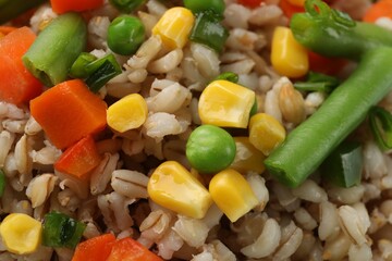 Tasty pearl barley porridge with vegetables as background, closeup