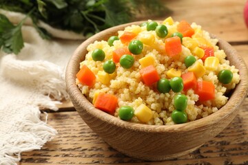 Tasty millet porridge with vegetables in bowl on wooden table, closeup