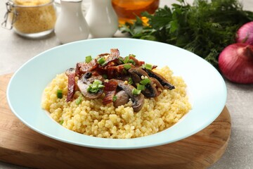 Tasty millet porridge with mushrooms, bacon and green onion on grey table, closeup