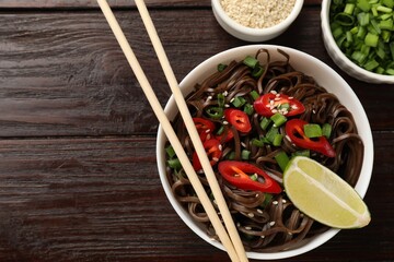 Tasty buckwheat noodles (soba) with chili pepper and sesame served on wooden table, flat lay. Space for text