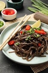 Tasty buckwheat noodles (soba) with chili pepper, onion and chopsticks on grey table, closeup