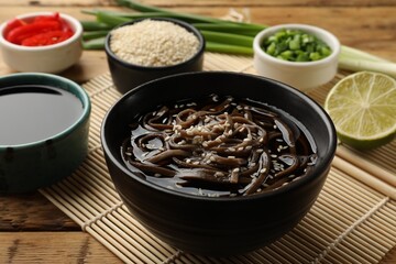 Tasty soup with buckwheat noodles (soba) and sesame in bowl on wooden table, closeup