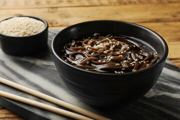 Tasty soup with buckwheat noodles (soba), sesame and chopsticks on table, closeup