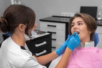 Female dentist performs an examination of the patient's oral cavity with the help of instruments in...