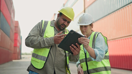 Two industrial workers in hardhats using tablet working together in container yard. Cargo shipping...