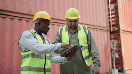 Two male container engineers working on tablet inspecting containers around a shipping yard of...