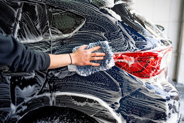 Professional car wash. Worker washes the vehicle body with foam. Stock photo - 715411065