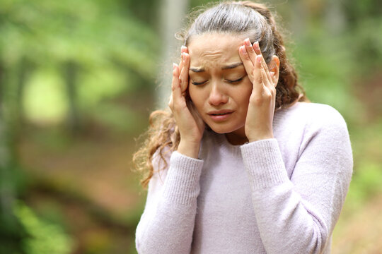 Worried woman suffering migraine in a forest