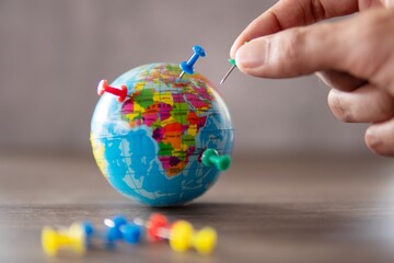 Closeup image of hand putting pins on world globe. Travel destination, planning vacation concept.