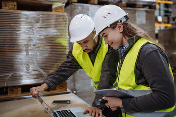 Warehouse manager talking with logistics employee in warehouse, planning transport of products,...