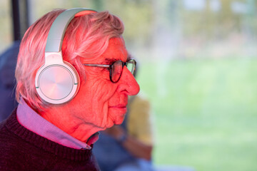 This image features a profile view of an elderly man gazing out of a window, lost in thought. He wears a pair of modern, over-ear headphones and a burgundy sweater, which suggests a blend of
