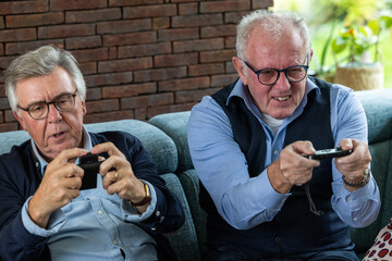 This lively image captures two senior men deeply engrossed in playing video games, their faces...