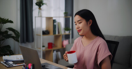 Portrait of Young woman holding coffee to drinking while working on the table in living room at home office.