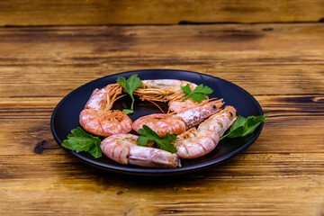 Plate with prepared shrimps and parsley leaves on a wooden table