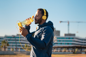 Athletic man with yellow headphones drinking water while working out.