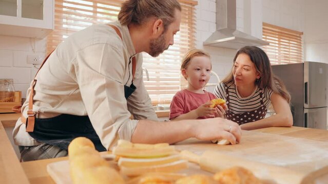 Happy family consists of father mother and little son kneading dough together in the kitchen. Caucasian parents teaching son to prepare dough for cookies and enjoying spending free time in kitchen.