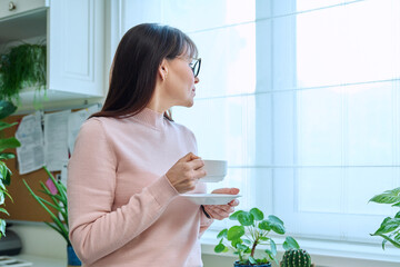 Middle-aged woman with a cup of coffee in her hands looks out window