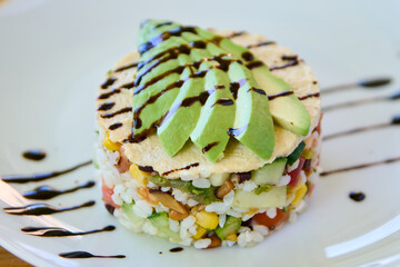 Avocado tartare with rice and vegetables on a white plate.
