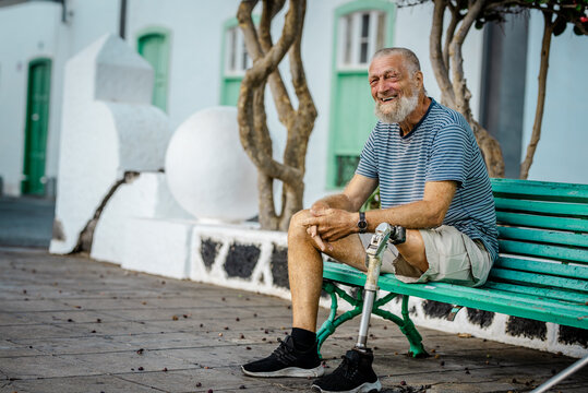 Elderly man with prosthetic leg. left rests sitting on a park bench. Spending a relaxing afternoon. People concept