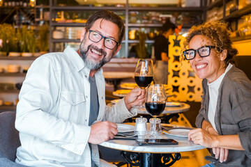 Happy couple smiling and talking in a restaurant drinking red wine - Married couple having lunch break at cafe bar - Lifestyle concept with man and a woman going out on weekend day