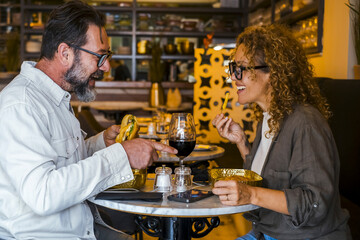 Happy couple smiling and talking in a pub restaurant eating burgers and chips - Married couple having lunch break at cafe bar - Lifestyle concept with man and a woman going out on weekend day