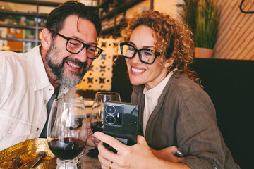 Happy couple smiling and talking in a restaurant looking at cell phone - Married couple enjoying lunch break at cafe bar - People and technology concept