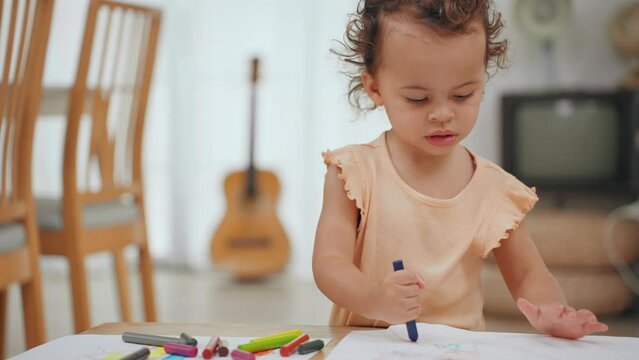 Little cute girl stand alone drawing and coloring with crayons in paper on table in living room at home. Learning of childhood.