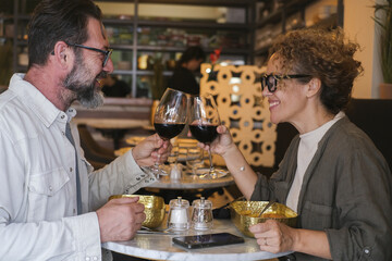 Happy couple smiling and talking in a restaurant drinking red wine - Married couple having lunch break at cafe bar - Lifestyle concept with man and a woman going out on weekend day
