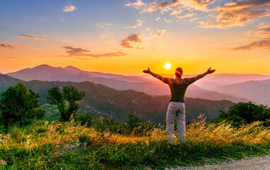 rejoicing man with beautiful scenic mountain sunset landscape on background. happy man watching...