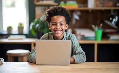 a small black boy working on his laptop computer at a desk with a smile