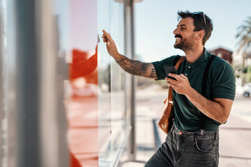 A young man is looking at time table at bus stop.