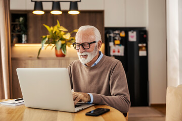 A happy senior executive is sitting at home and typing on a laptop while working remotely form home.