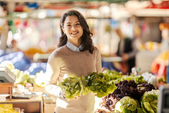 Portrait of a happy woman shopping fresh vegetables and choosing lettuce at farmers market.