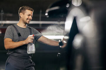 A car wash worker is spraying detergent and cleaning a car.