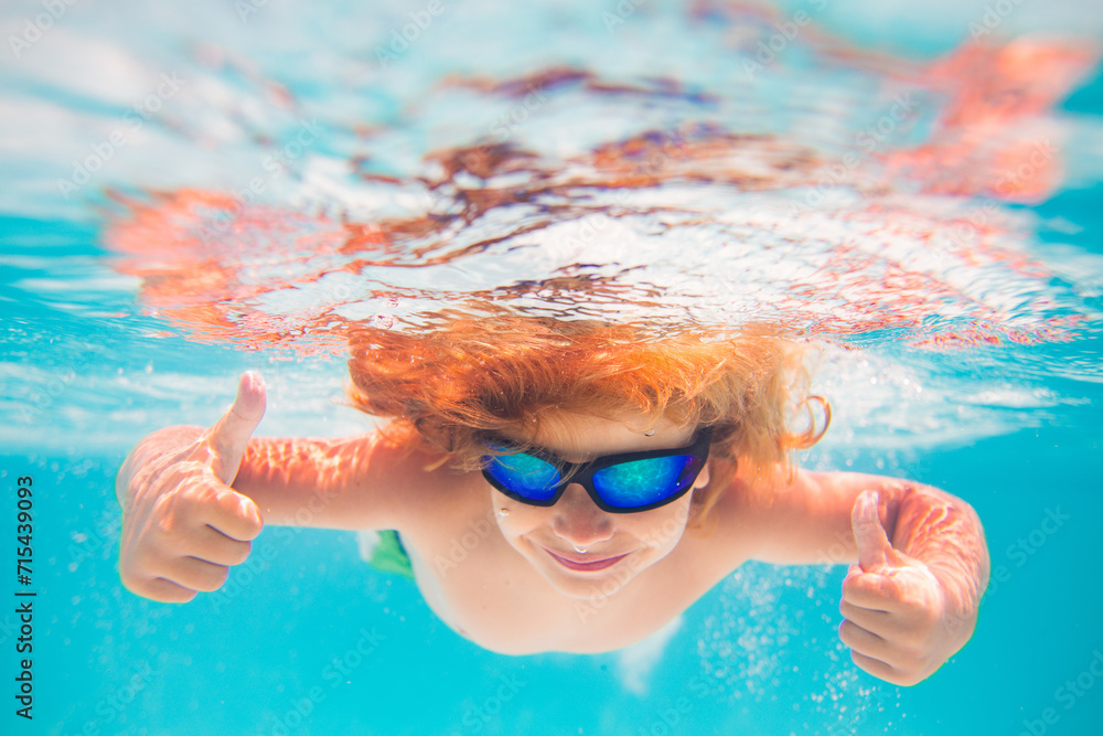 Wall mural child in swimming pool underwater with thumbs up. underwater kid swim in pool. child boy swimming an