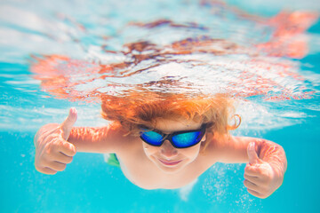 Child in swimming pool underwater with thumbs up. Underwater kid swim in pool. Child boy swimming...