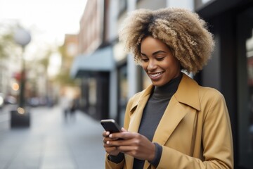 blonde african american woman looking at a smartphone walking along a city street. - obrazy, fototapety, plakaty