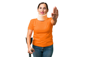 Middle-aged caucasian woman wearing neck brace over isolated background making stop gesture