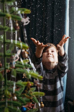 Playful boy catching fake snow near Christmas tree at home