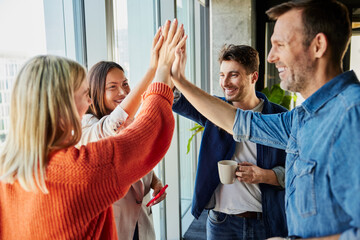 Happy businessmen and businesswomen giving high-five together in office