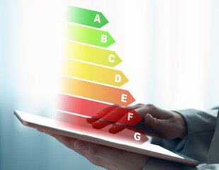 Energy efficiency rating coming out of tablet. Man using device on light background, closeup
